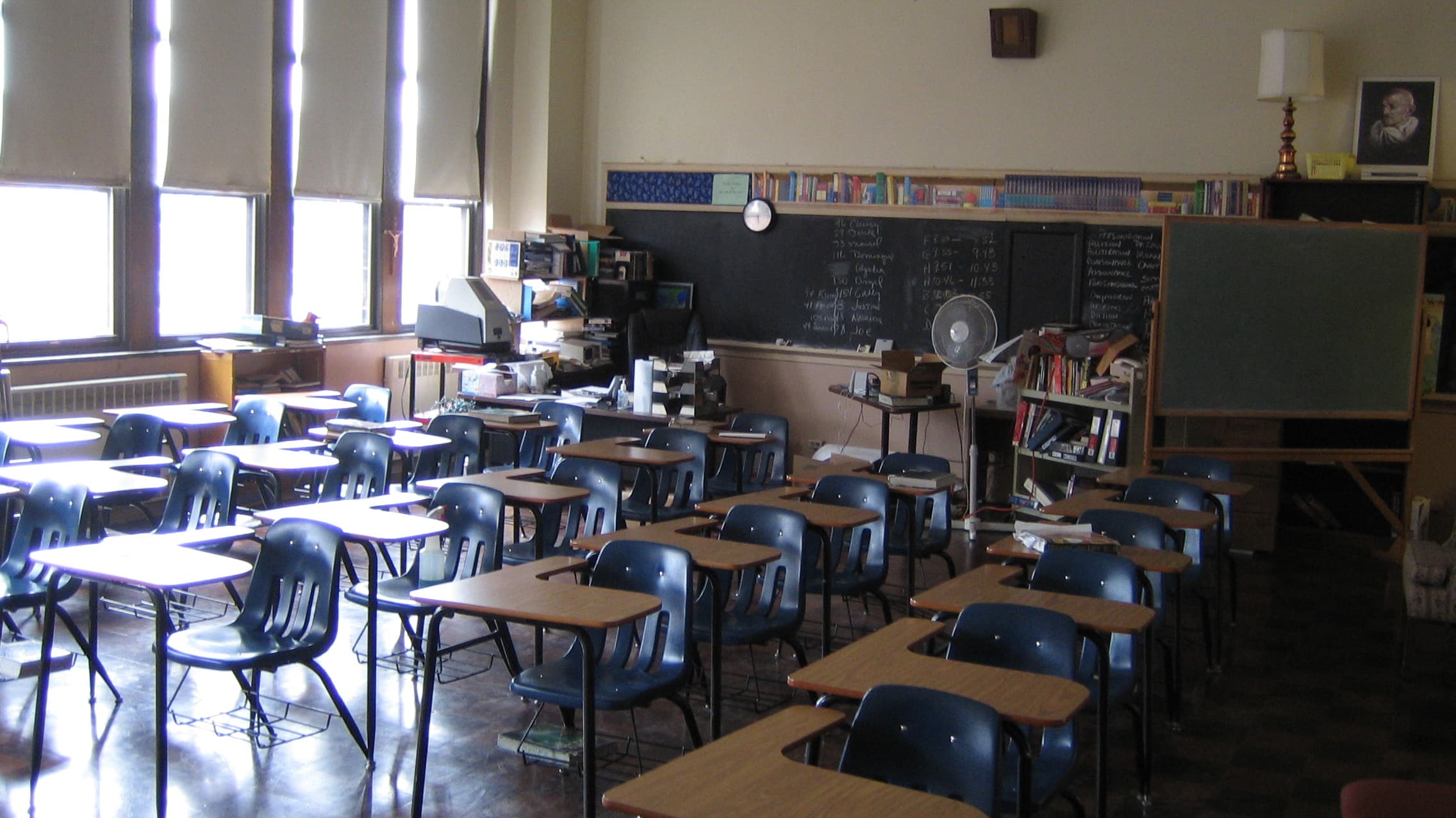 An empty public school classroom with rows of vacant student desks facing a chalkboard.