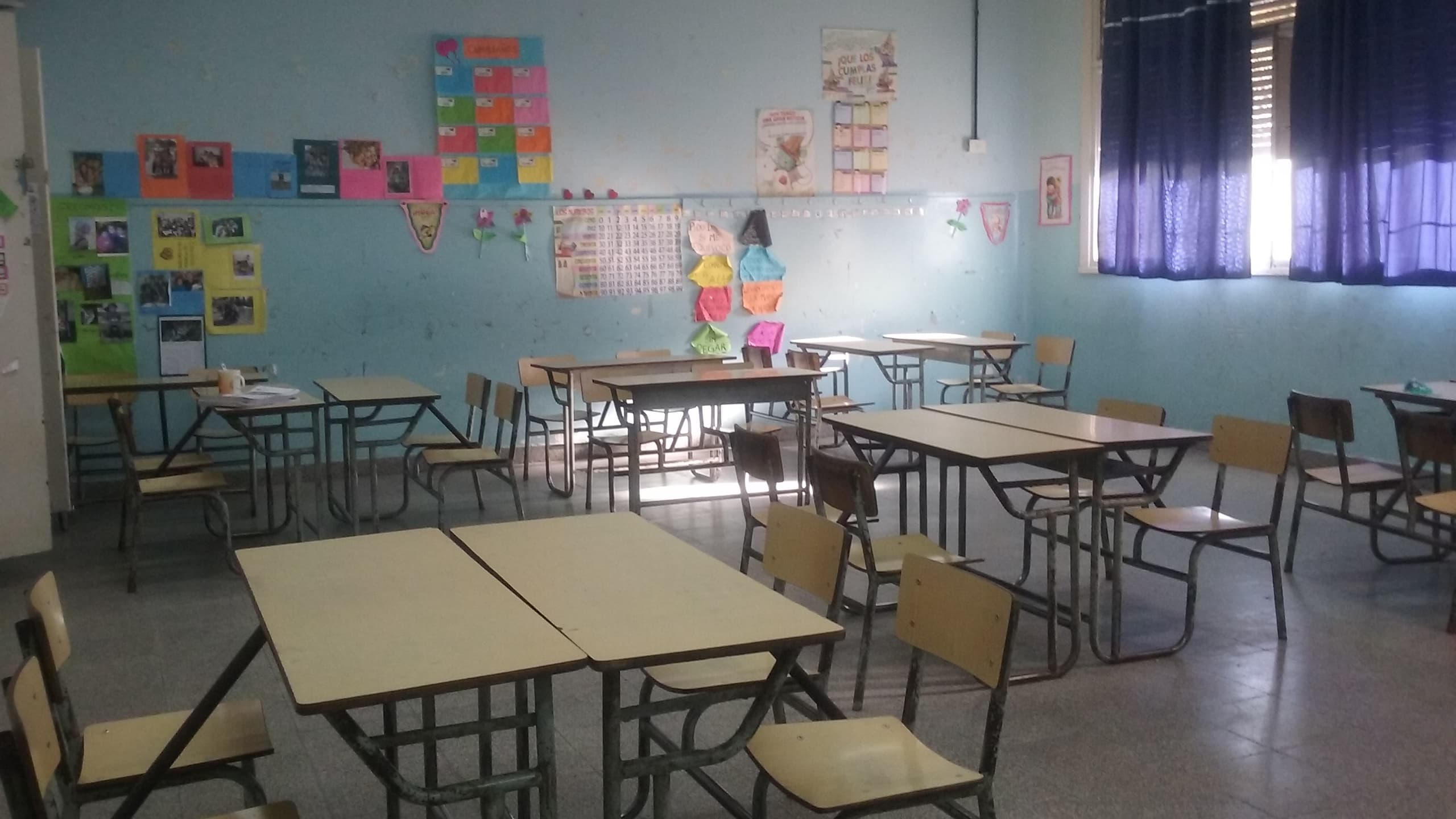Rows of empty wooden student desks and chairs in a quiet, unoccupied classroom
