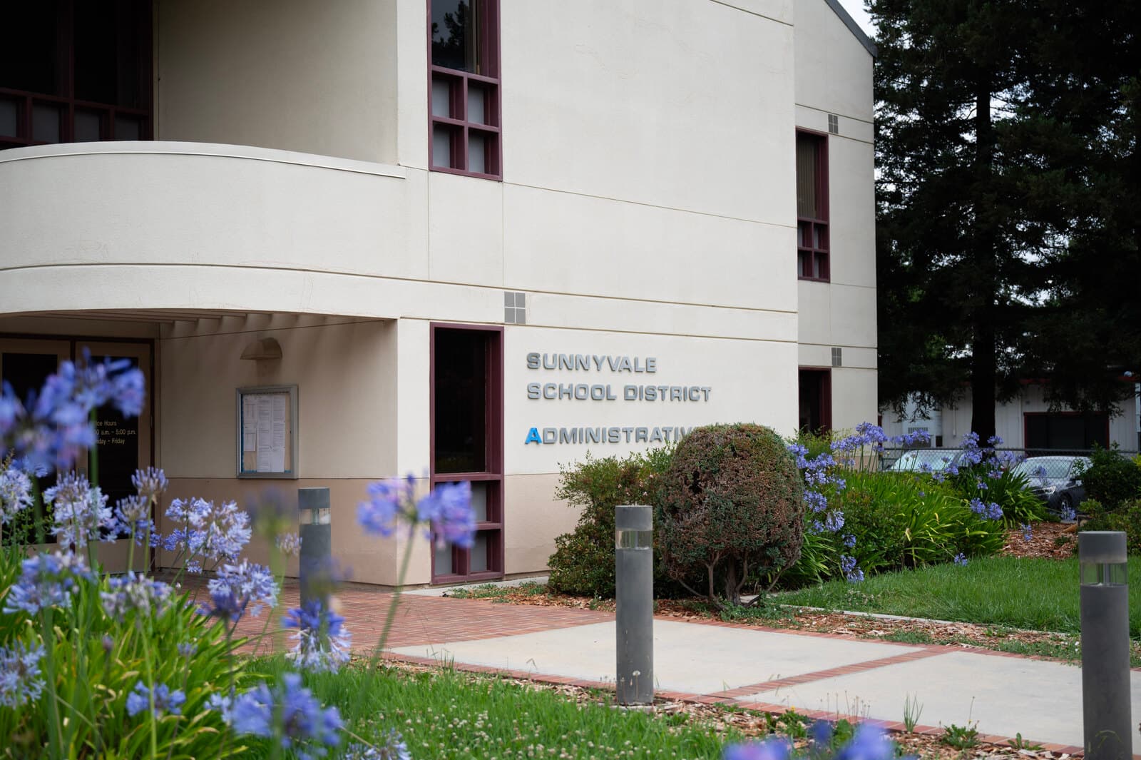 The Sunnyvale School District Administrative building, with the district name on its exterior wall, framed by purple flowers and trees